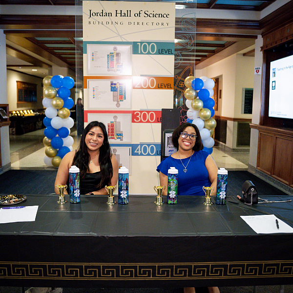 Students sit and smile at welcome desk for Galvin Scholars Gormal 2024