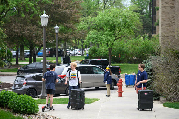 Students with suitcases chat on sidewalk during Move Out Week